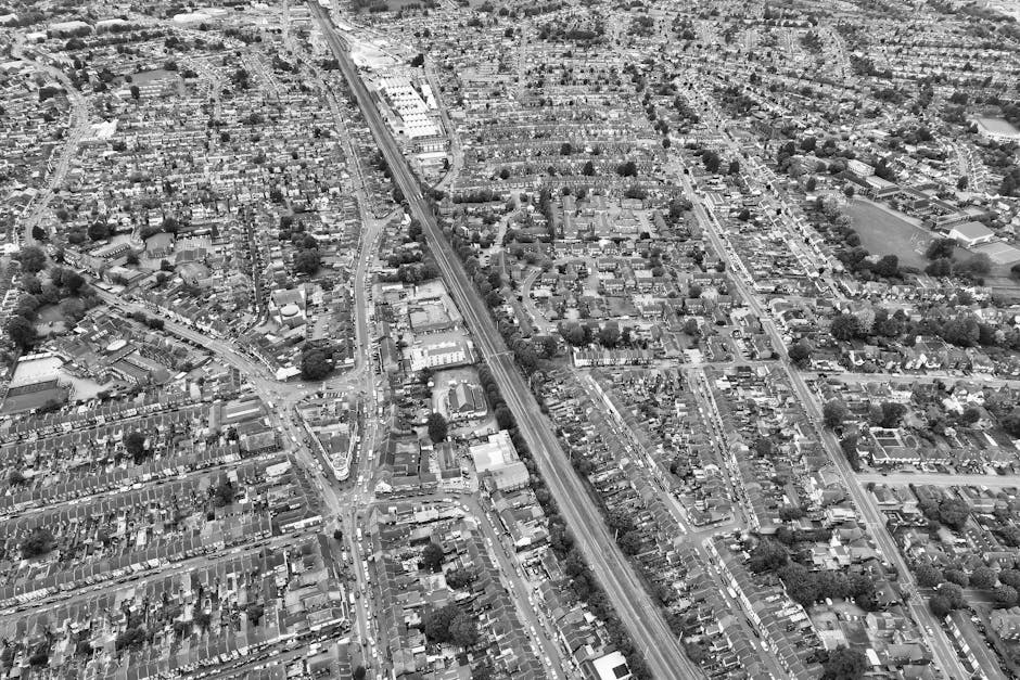Aerial black-and-white view of a suburban neighbourhood featuring densely packed houses with small gardens, narrow streets, and intersecting roadways. A railway line runs diagonally across the image, 