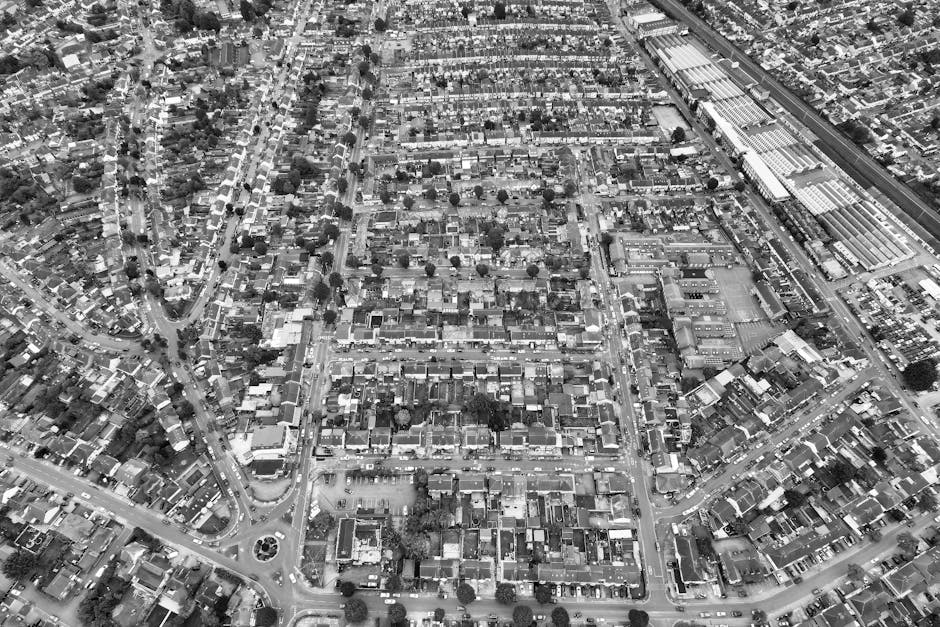 Aerial black-and-white view of a suburban neighbourhood featuring densely packed houses with small gardens, narrow streets, and intersecting roadways. A railway line runs diagonally across the image, 