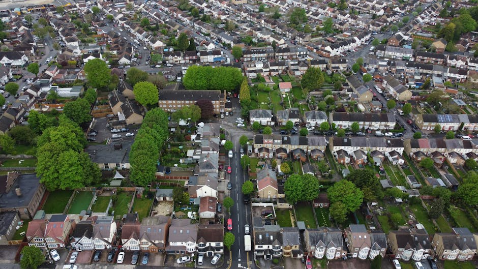 An aerial view of a residential neighborhood displaying a variety of gardens and yards attached to individual houses. The gardens feature well-maintained lawns with neatly trimmed grass, flower beds,