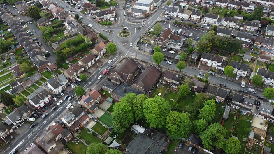 An aerial view of a residential neighborhood displaying a variety of gardens and yards attached to individual houses. The gardens feature well-maintained lawns with neatly trimmed grass, flower beds,